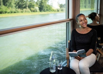 Solo traveler reading near a wide window on a river ship
