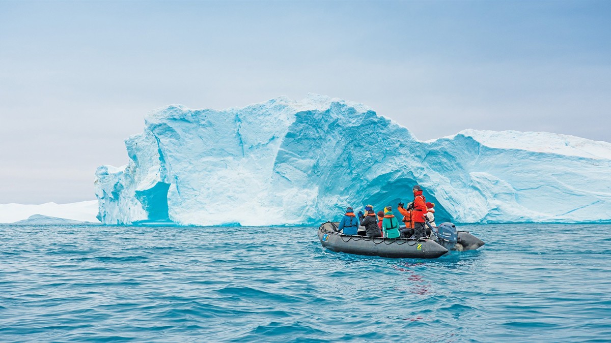 A Lindblad Expeditions ship, the Greg Mortimer, with Zodiacs in the water nearby, surrounded by icebergs and mountains