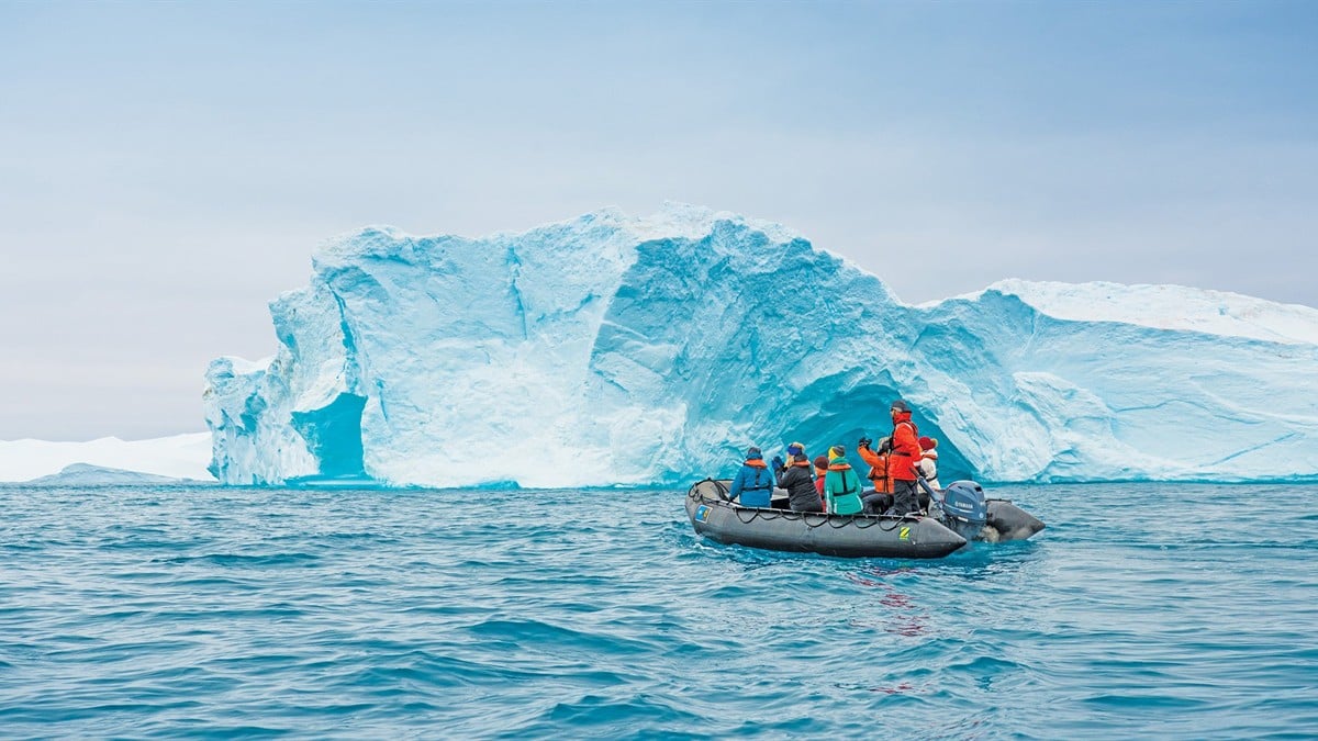 Lindblad Expeditions ship navigating a pristine Alaskan fjord with a waterfall cascading down a lush green mountain