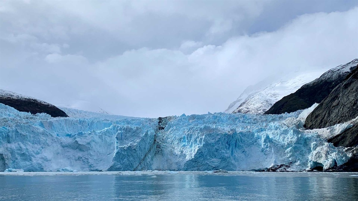 The Greg Mortimer expedition ship sailing through ice-strewn waters with Zodiac boats deployed nearby