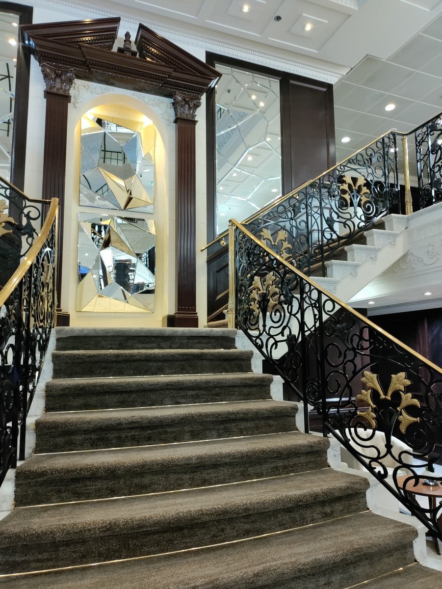 The elegant grand staircase and warm classical wood decor of the Azamara Onward atrium
