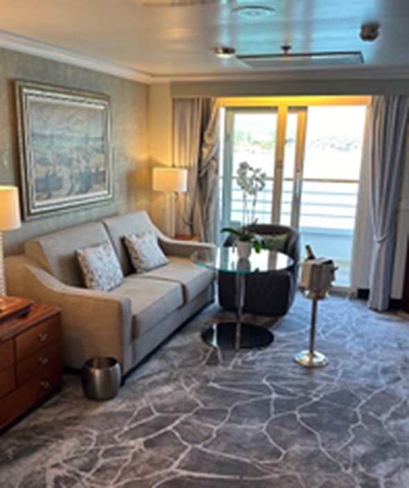 Spacious living room of the Sapphire Veranda Suite aboard Crystal Symphony with sofa, glass table, fresh orchids, chilled champagne, and veranda doors