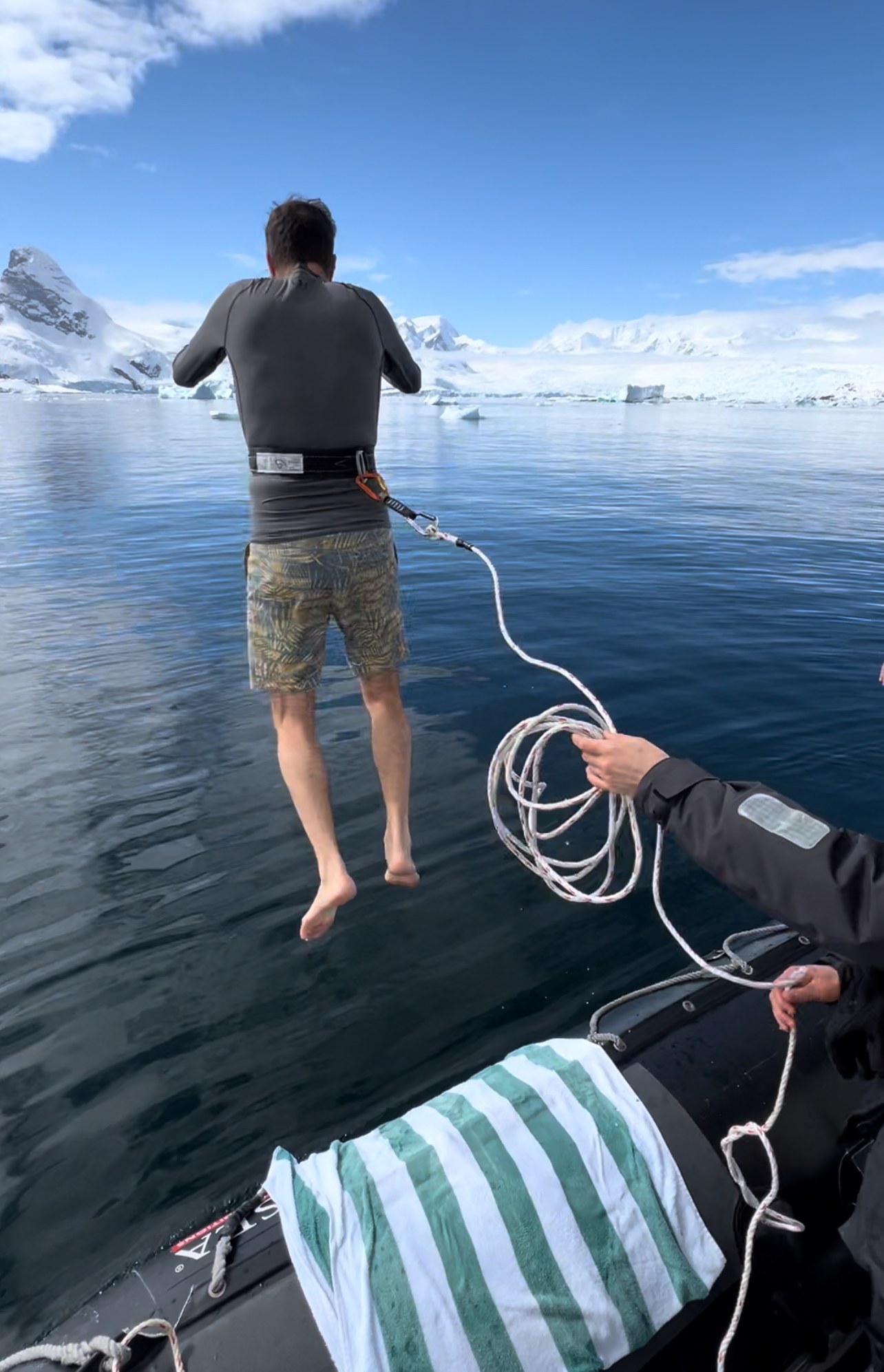 Expedition traveler leaping into sub-zero Antarctic ocean water with safety tether harness from Zodiac tender