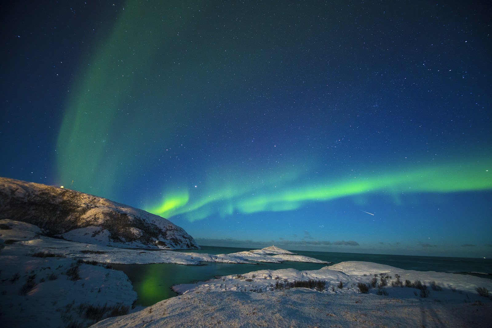 Shooting star streaking through vivid green Aurora Borealis in clear Arctic night sky