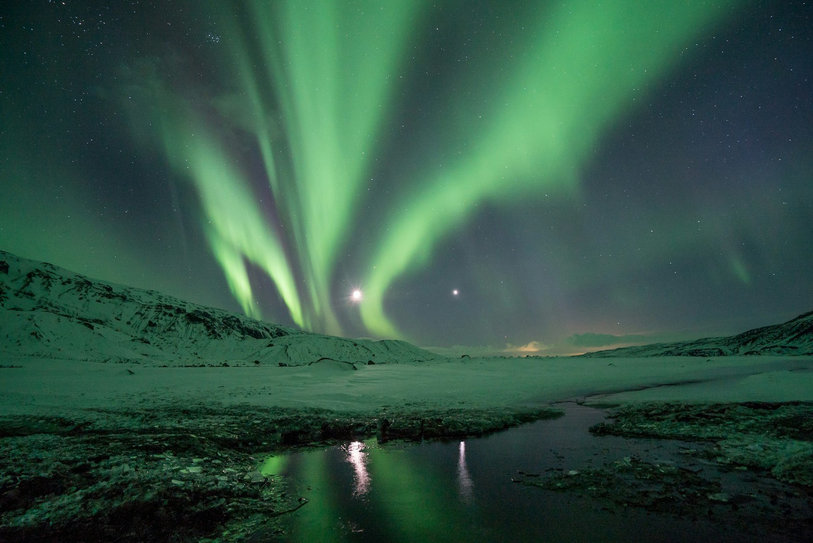 Emerald Northern Lights arching over rugged volcanic landscape in Iceland