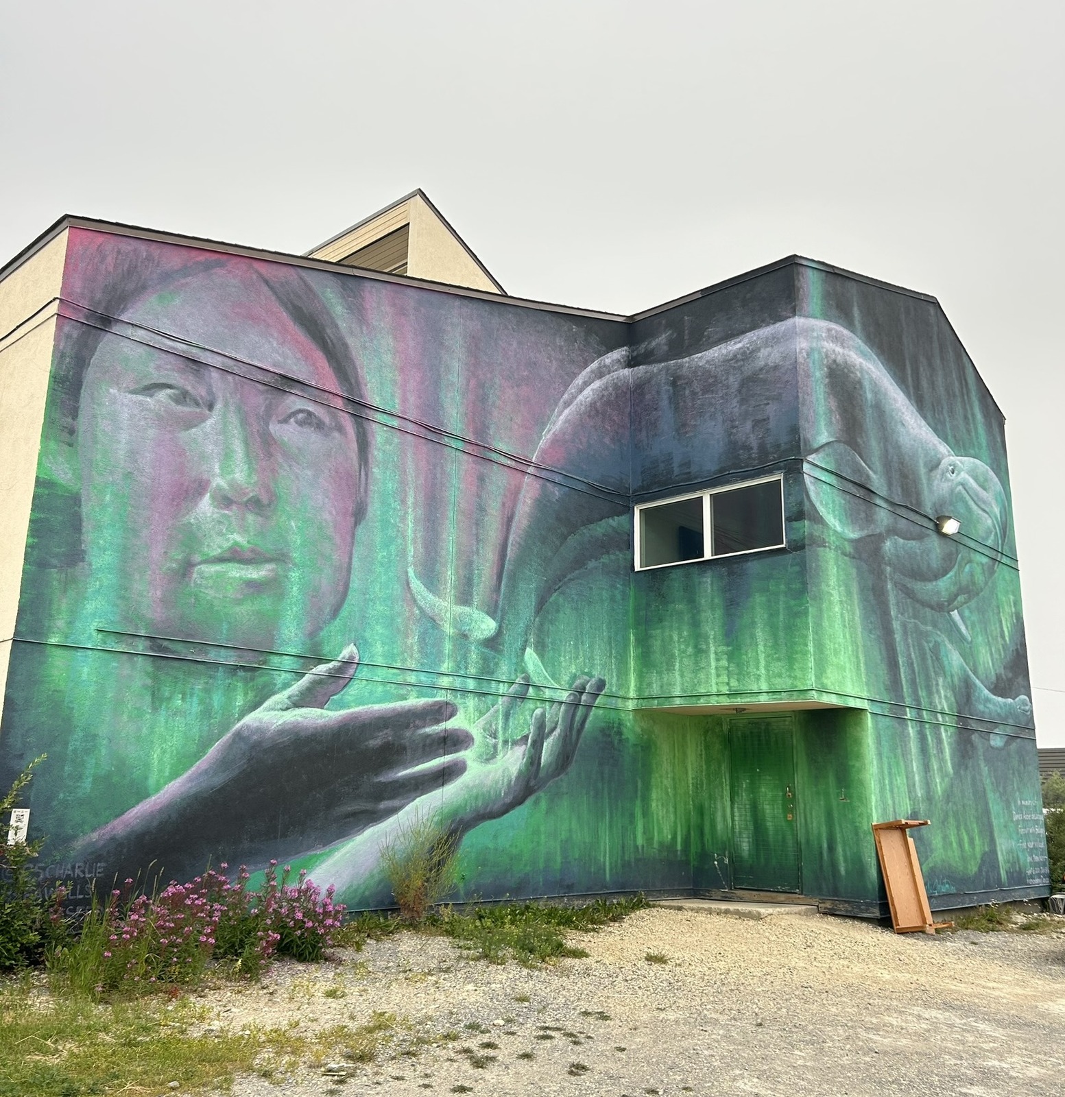 Vibrant SeaWalls public art mural in Churchill featuring an Indigenous woman, a beluga whale, and green northern lights with blooming fireweed