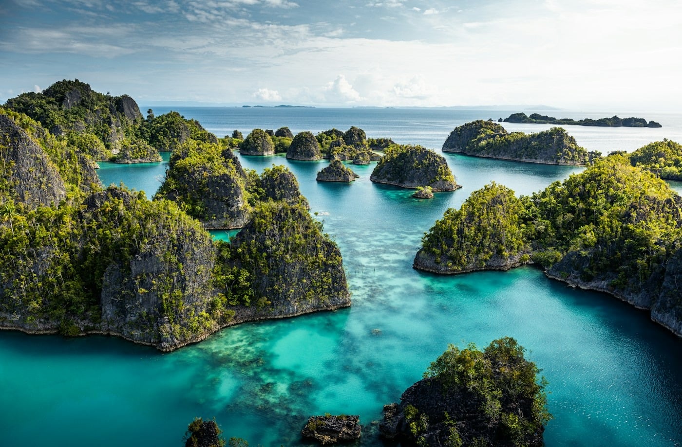 Aerial perspective of turquoise water and forested limestone islets in Raja Ampat