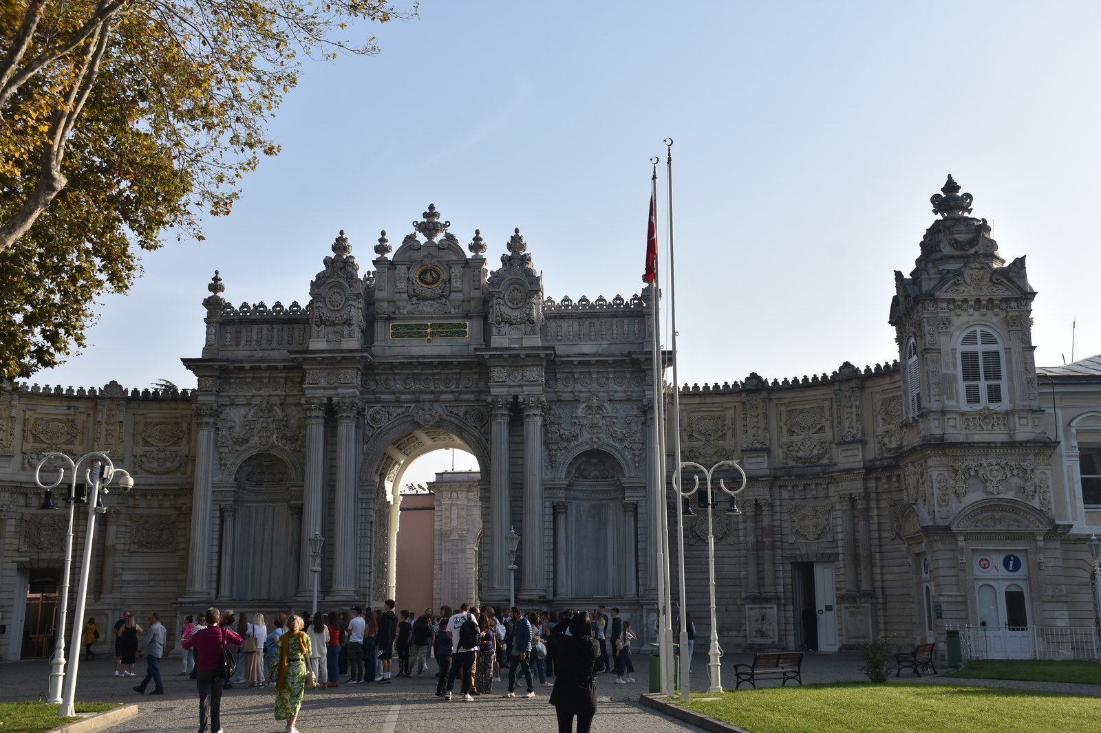 Monumental white baroque imperial gate of Dolmabahce Palace framed by manicured gardens