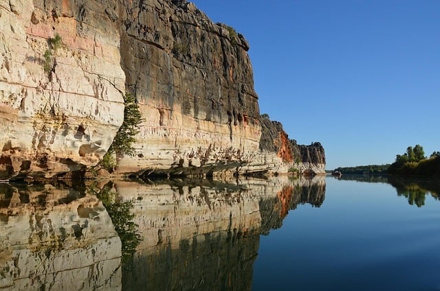 Towering red sandstone cliffs reflecting in the tranquil waters of a Kimberley river gorge