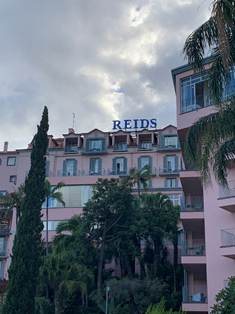 The iconic pink Victorian facade of Belmond Reid's Palace surrounded by subtropical palm gardens in Funchal