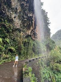 Traveler walking along a lush green Levada trail directly underneath a cascading mountain waterfall