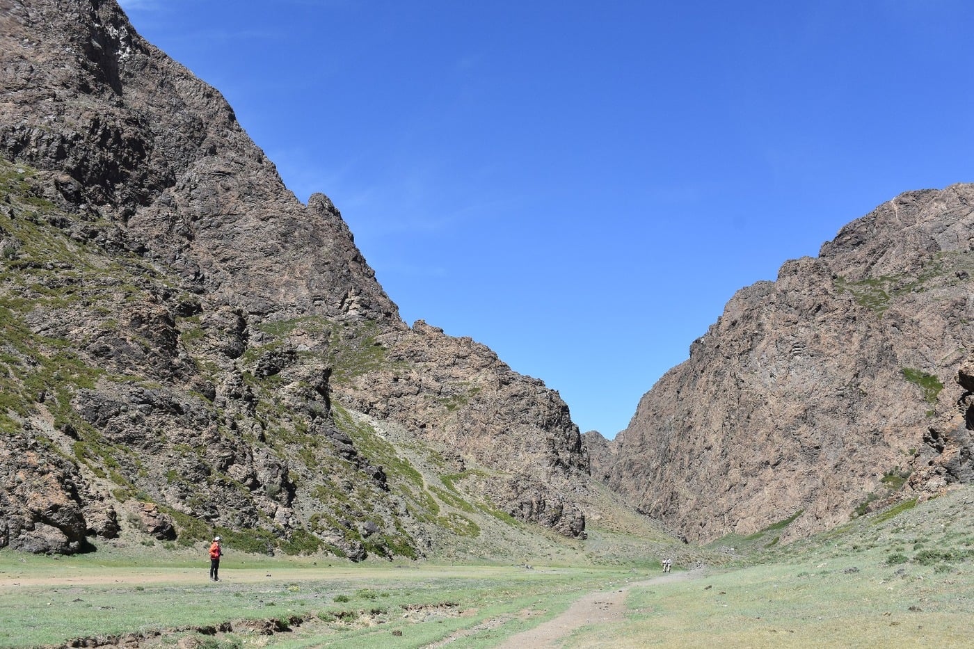 Hikers navigating the narrow, rocky gorge of Yolyn Am with patches of summer ice