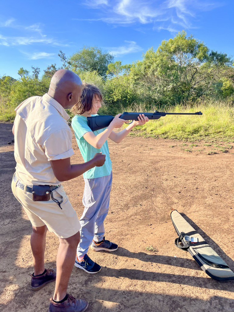 Karl Kannstadter son receiving air rifle target shooting lesson from guide Bongo in Phinda bushveld