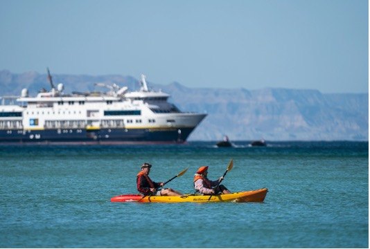 National Geographic Venture anchored in a secluded cove with kayakers