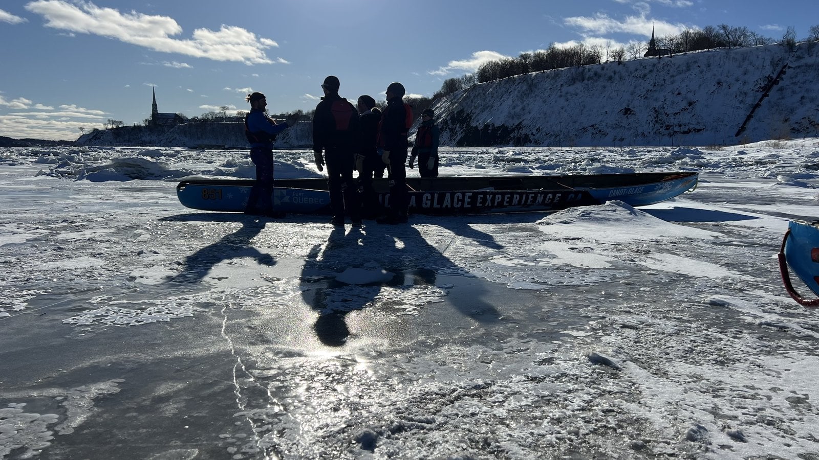 Canot a Glace Experience crew standing on ice blocks with cliff and church spire in background