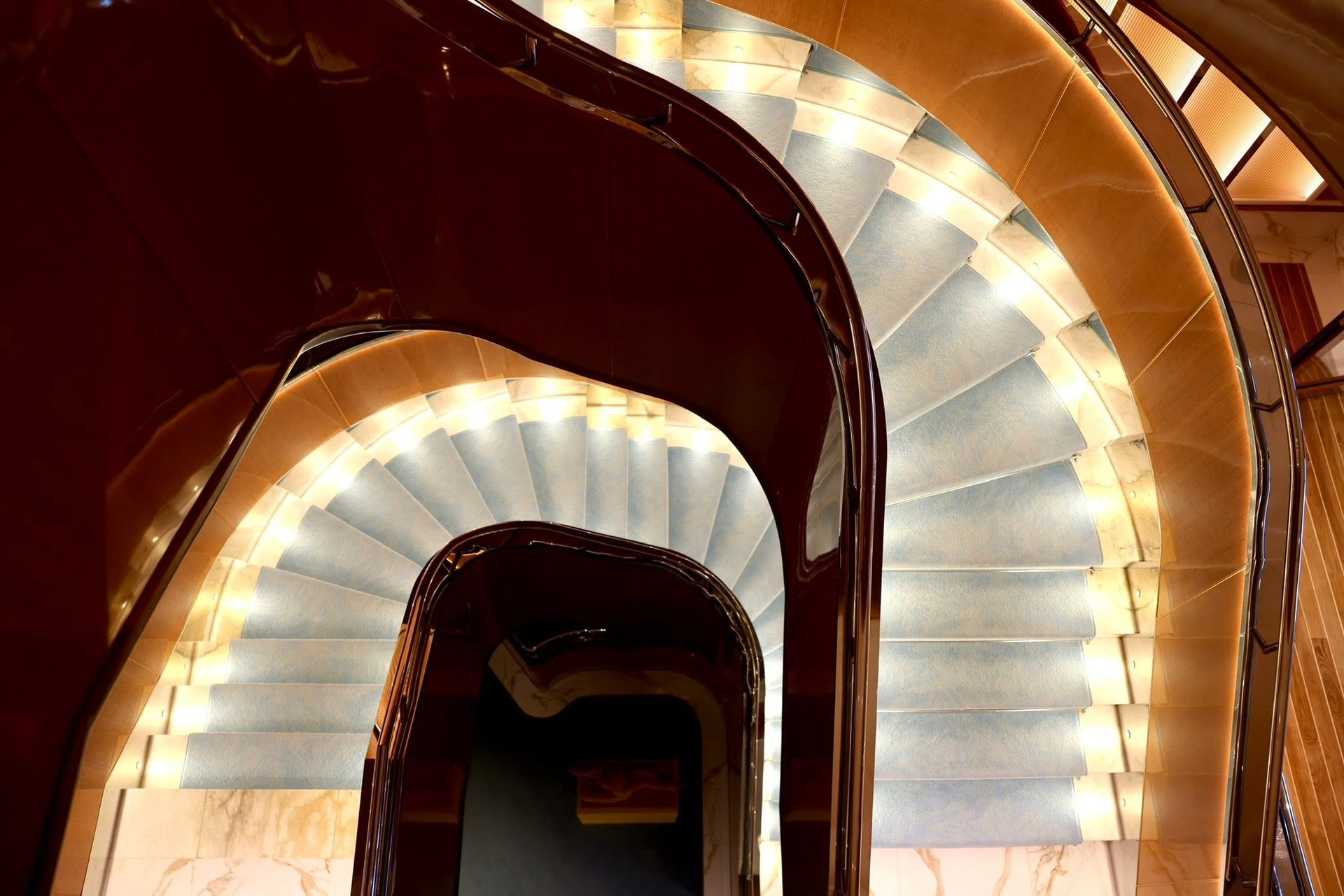 Dramatic illuminated spiral staircase connecting yacht passenger decks on Four Seasons Yachts