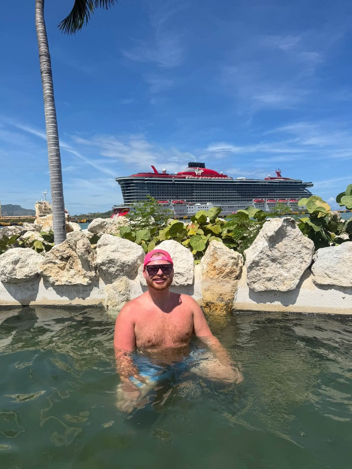 Logan White in oceanfront lagoon with Virgin Voyages ship in background