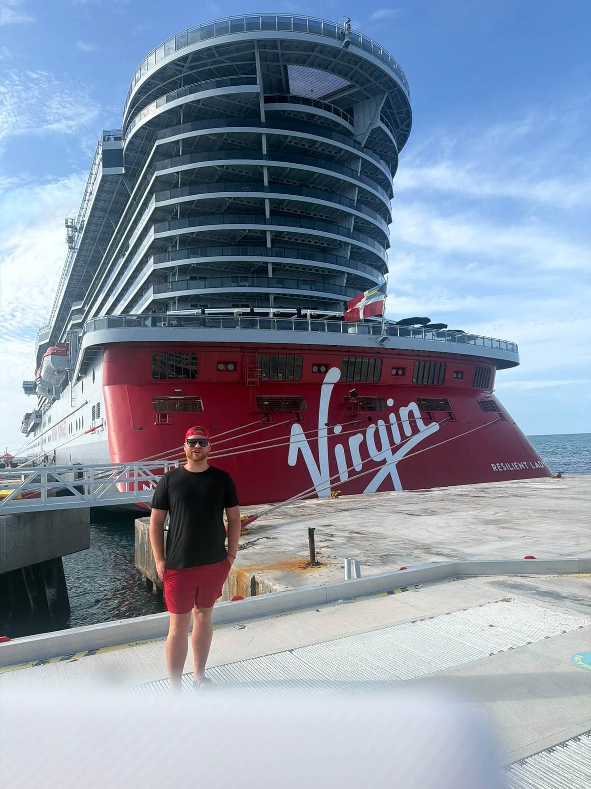 Logan White standing on the pier in front of Virgin Voyages Lady Ship