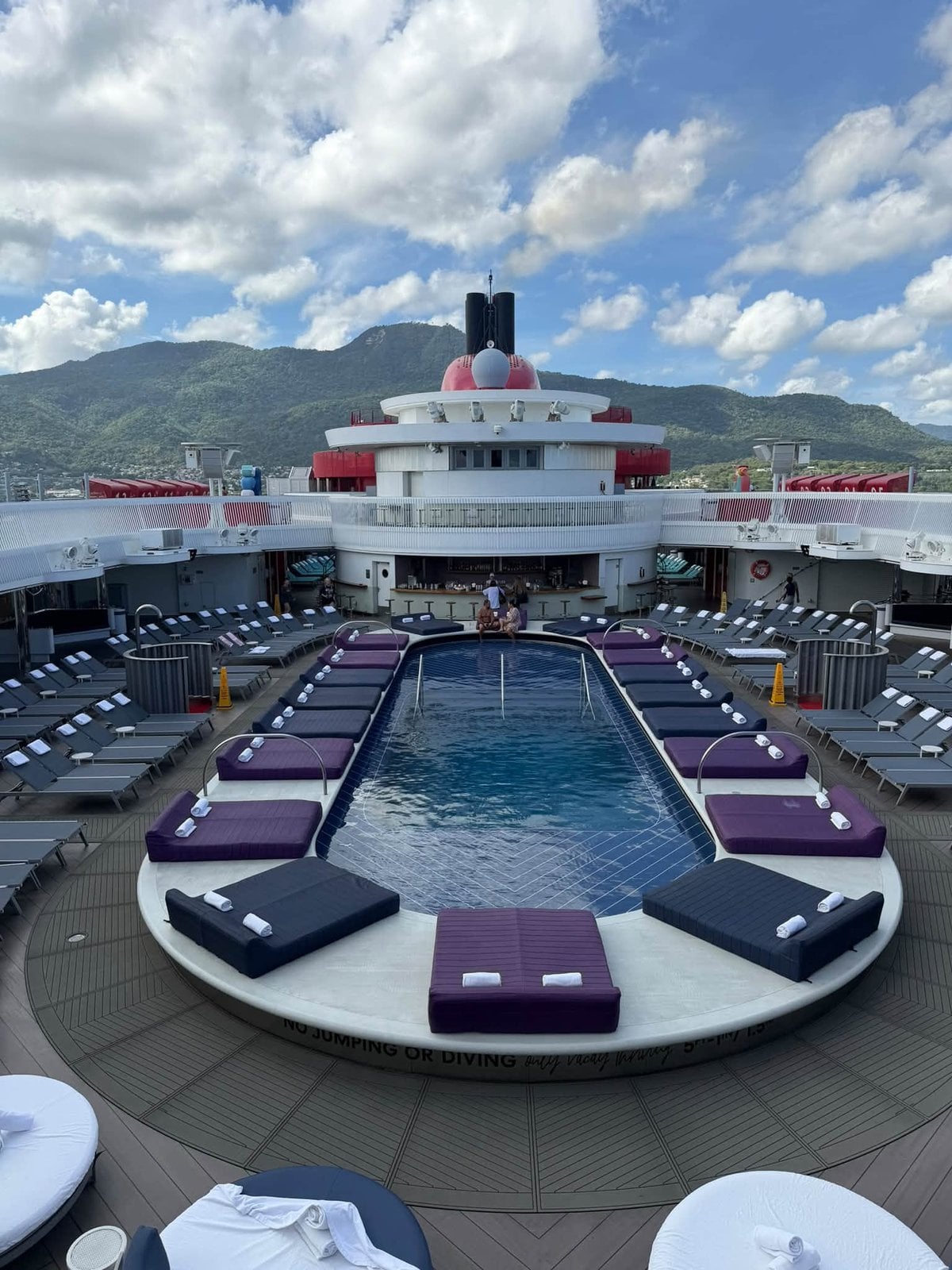 The sleek Aquatic Club pool deck, daybeds, and iconic red funnel aboard Scarlet Lady