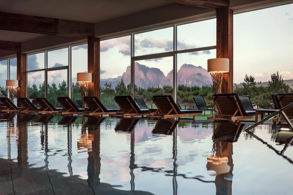 Heated indoor and outdoor panoramic pool framing Dolomite mountain peaks
