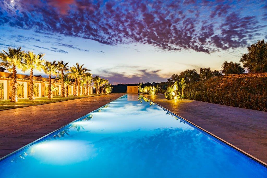 One Blue Pool surrounded by manicured lawns, sun cabanas, and baroque stone walls