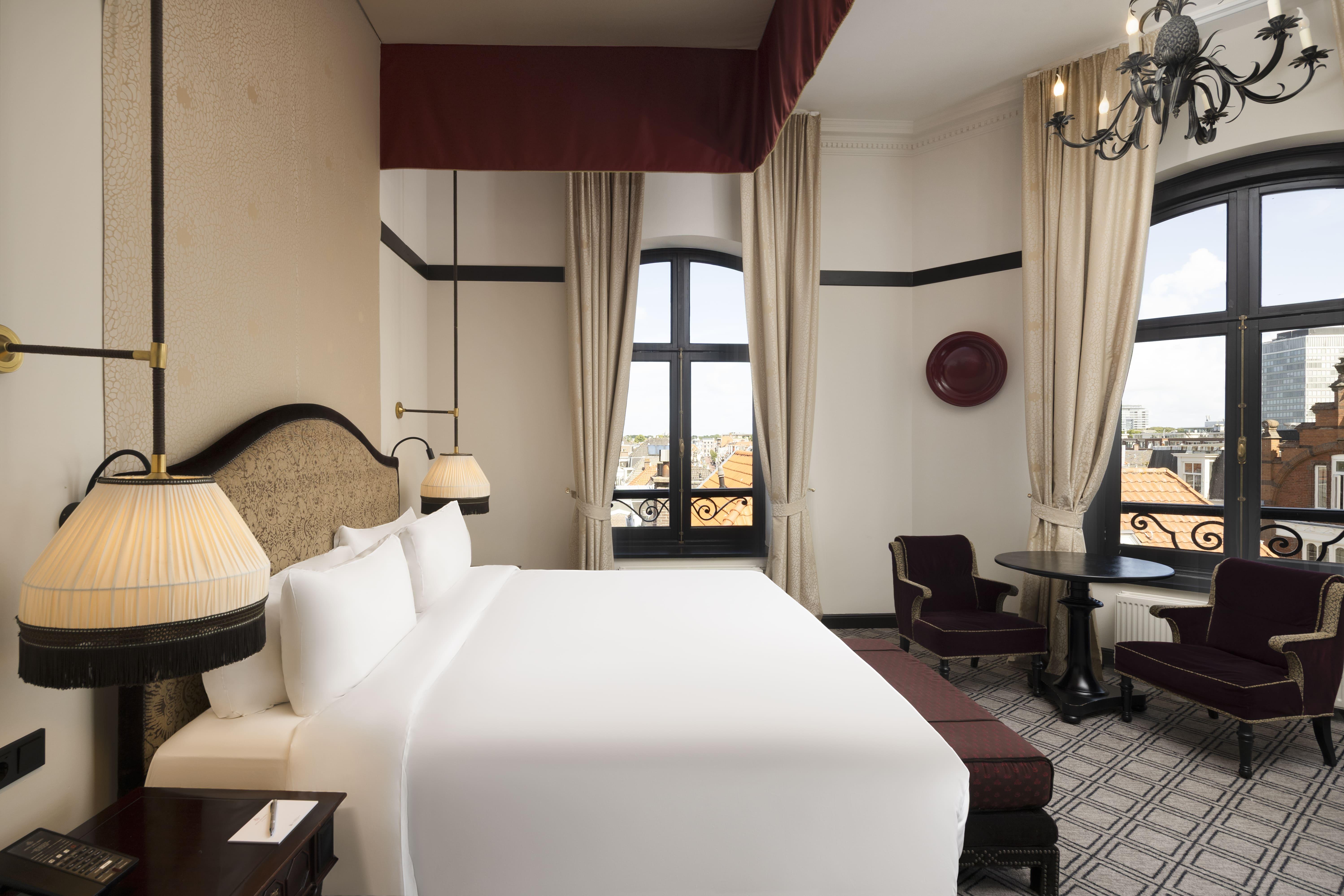 Executive guestroom featuring pineapple chandelier, plush canopy bedding, and marble bath