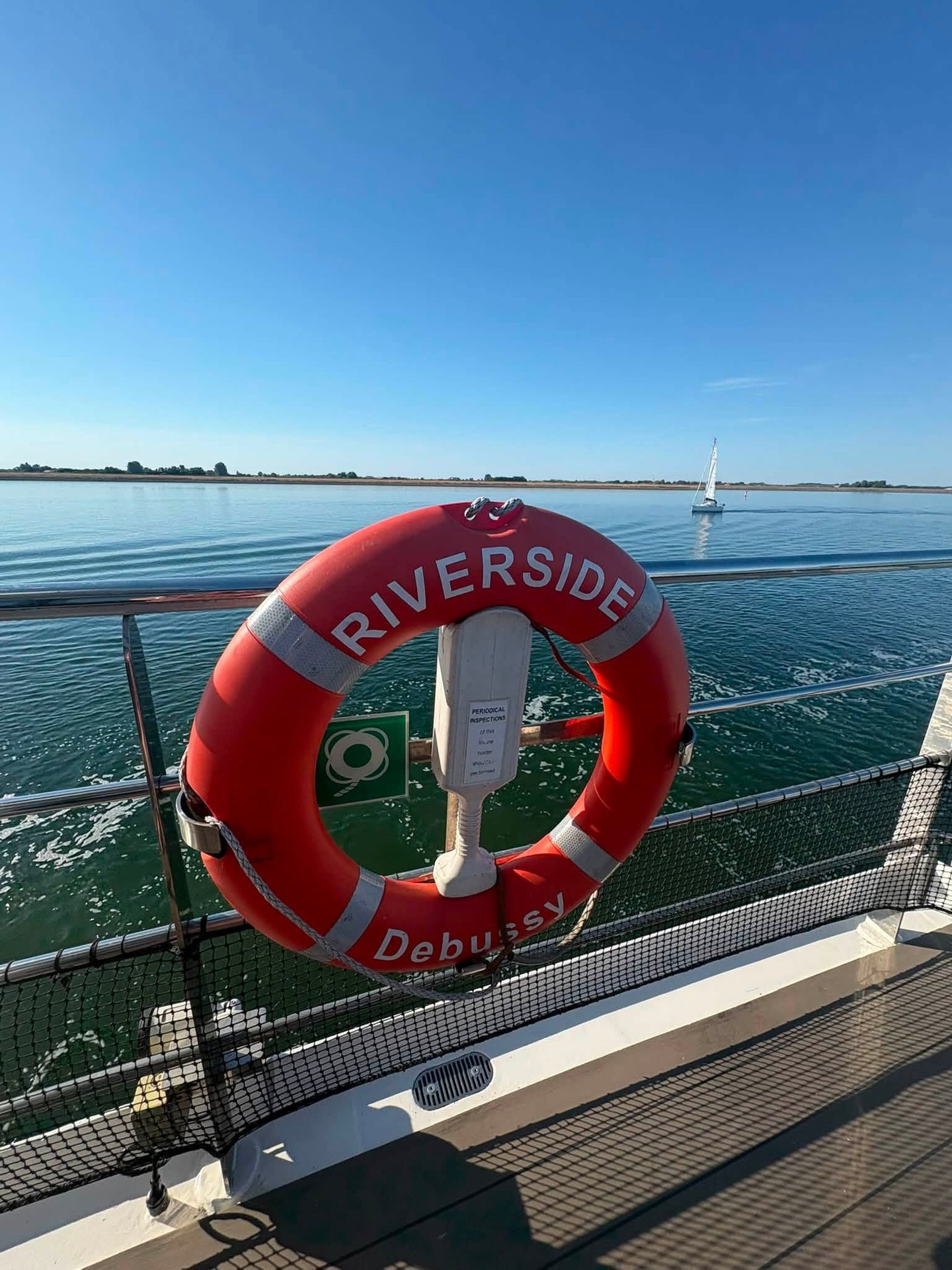 Riverside branded life ring against sparkling blue river waters and distant shoreline