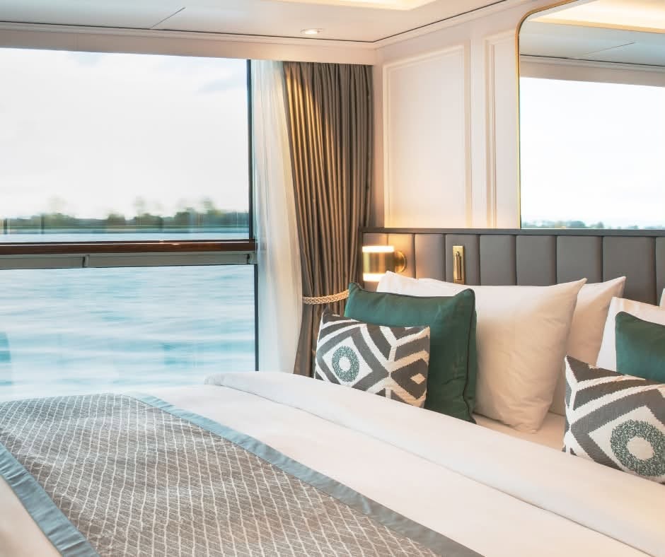 King bed with plush pillows directly facing drop-down floor-to-ceiling panoramic river window