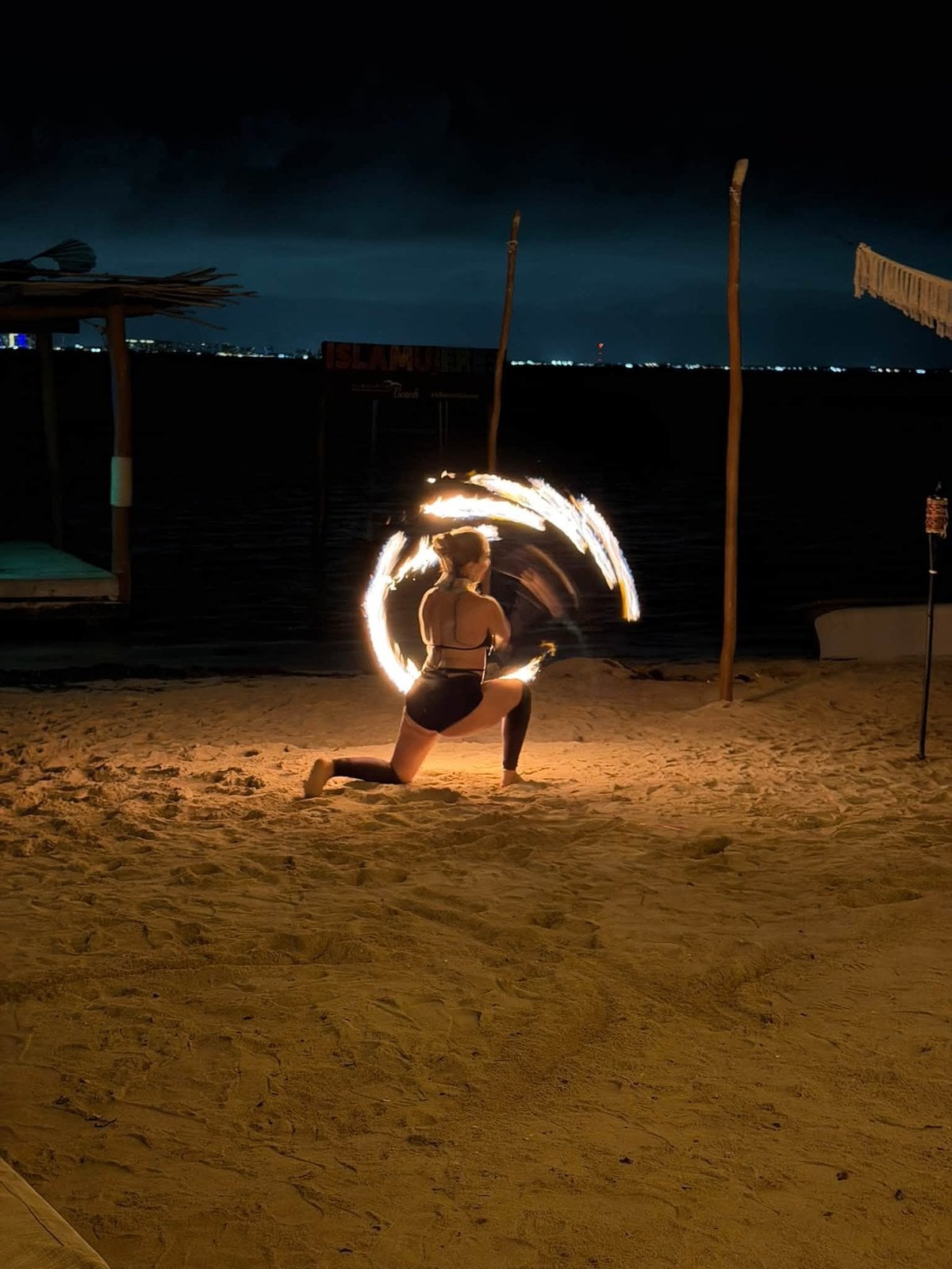 Dramatic live fire dancer spinning flaming rings on the beach at night on Isla Mujeres