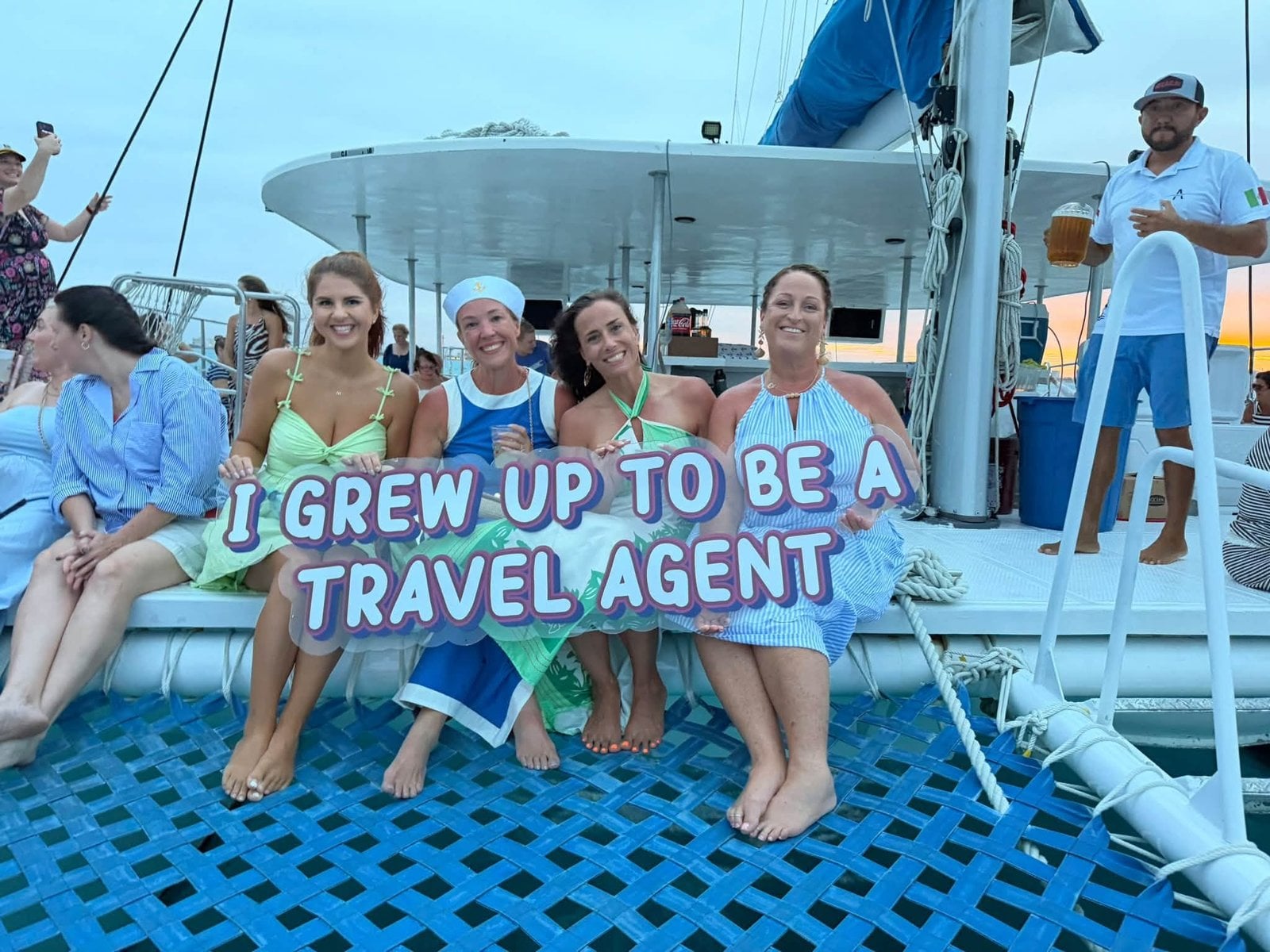 Vincent Vacations advisors relaxing on catamaran bow trampoline holding travel agent sign at sea
